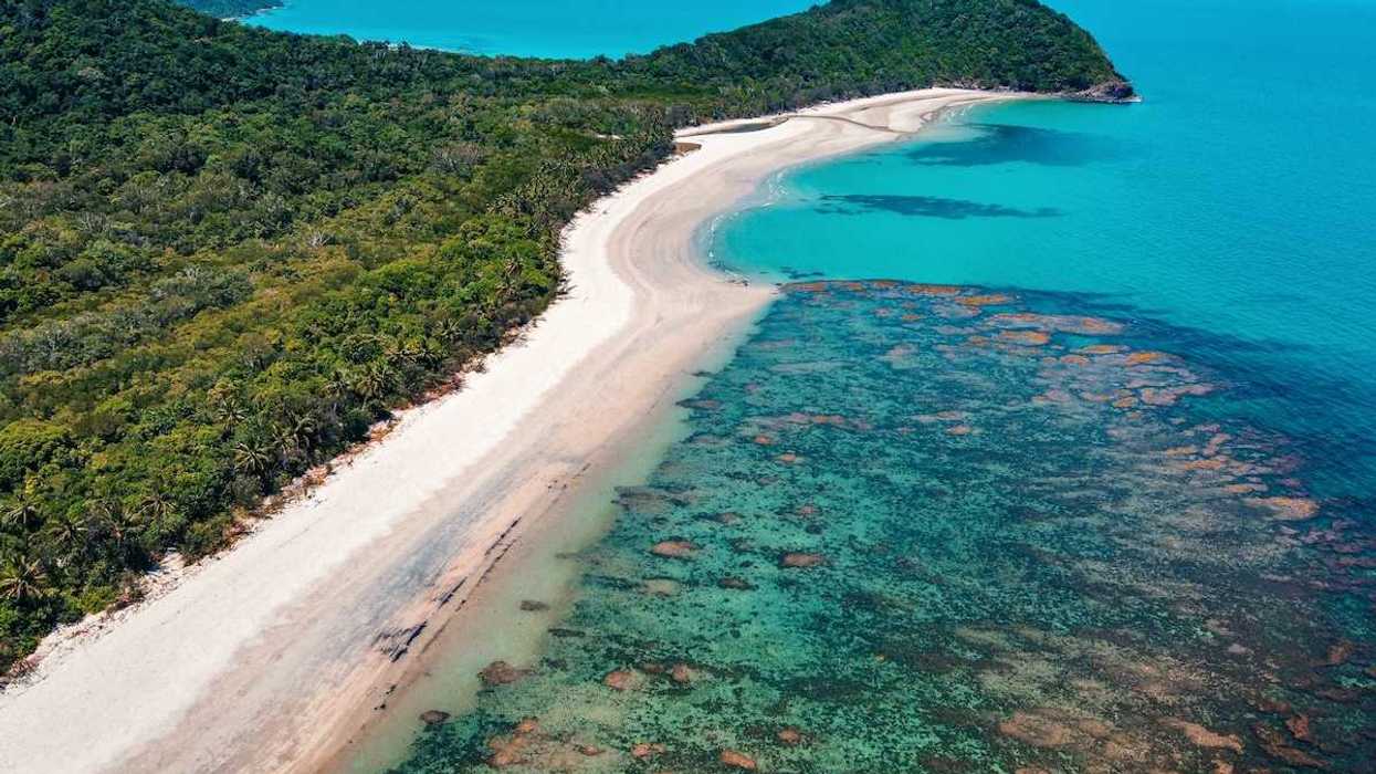 The Great Barrier Reef from above. Underwater, but visible, reef formation, with azure blue water and sky and land extendinginto ocean.