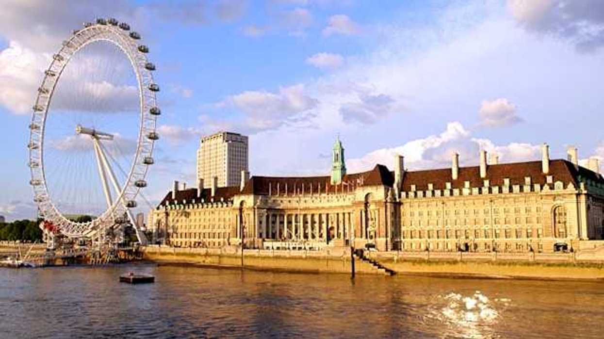The River Thames and ferris wheel next to a large building on a sunny day