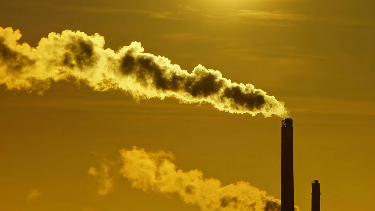 The sun is setting behind a factory with smoke coming out of it.