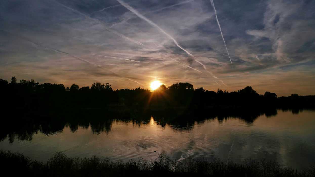 the sun is setting over a lake with contrails in the sky