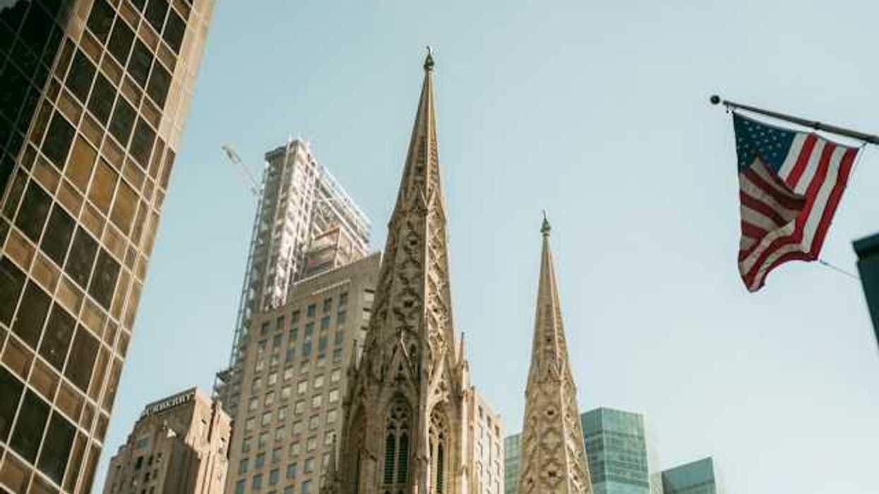 The top portion of a cathedral in a city with buildings surrounding it