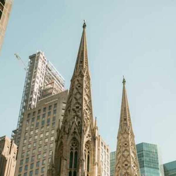 The top portion of a cathedral in a city with buildings surrounding it
