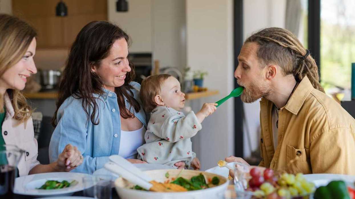 Three adults and a baby gathered around a table of fresh fruits and veggies implying healthy family eating