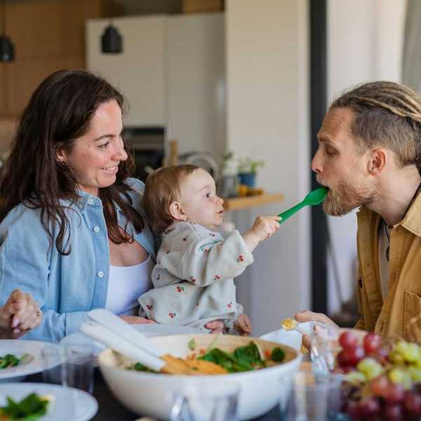 Three adults and a baby gathered around a table of fresh fruits and veggies implying healthy family eating