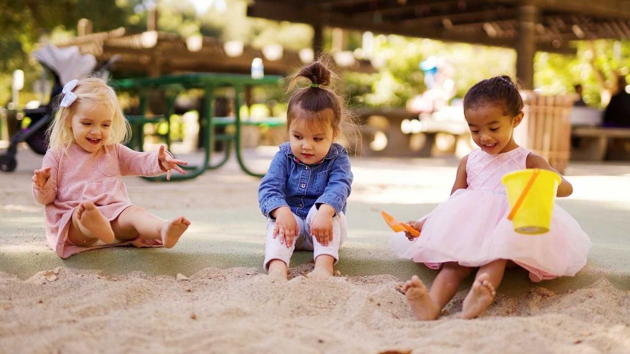 Three children sitting and playing in playground sand