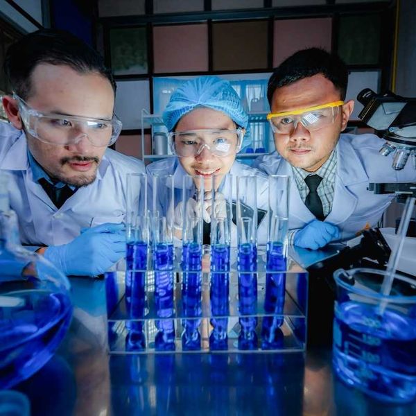 Three Chinese scientists scrutinizing six test tubes of blue liquid