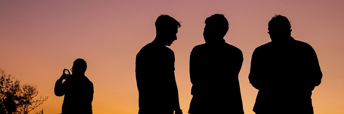 Three men silhouetted against a sunset