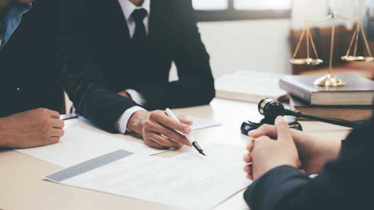 Three people sitting at a desk looking at paperwork with the scales of justice and a gavel to the side
