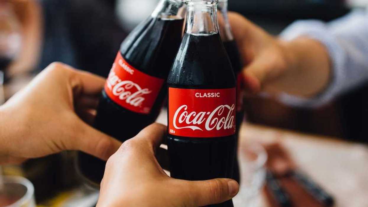 Three people, with only hands visible toasting with bottles of Coca Cola