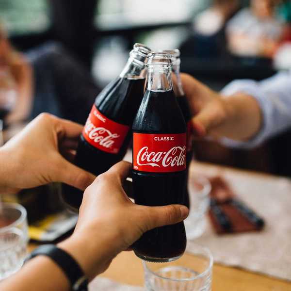 Three people, with only hands visible toasting with bottles of Coca Cola