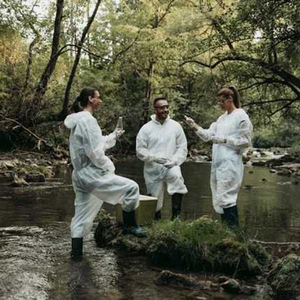 Three researchers in white coveralls standing in a creek