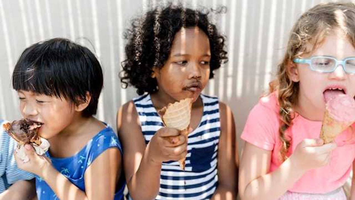 Three small children sitting in the shade eating ice cream