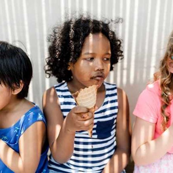 Three small children sitting in the shade eating ice cream