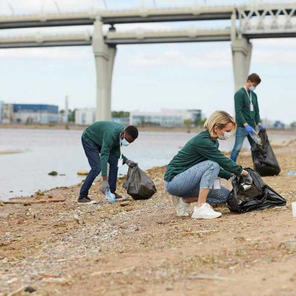 Three volunteers with garbage bags scour waterfront for trash