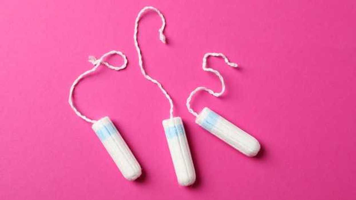 Three white tampons with strings sitting on a pink background