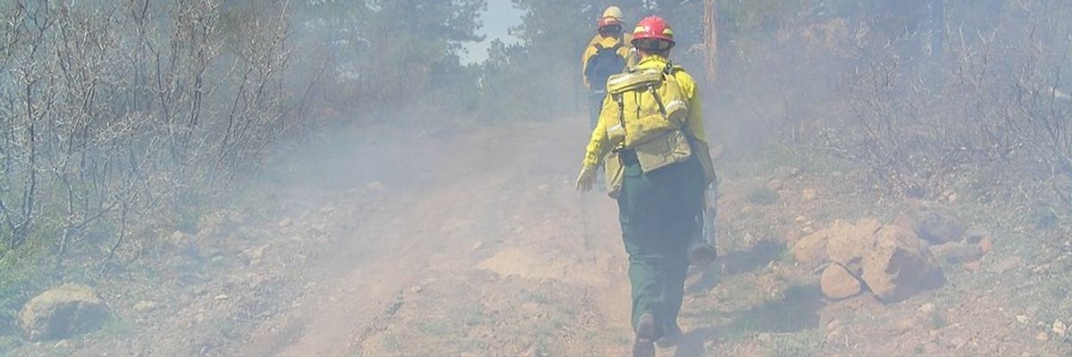 Three wildland firefighters hiking up a dirt road to a fire.