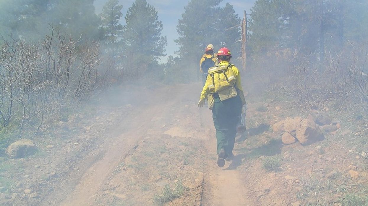 Three wildland firefighters hiking up a dirt road to a fire.