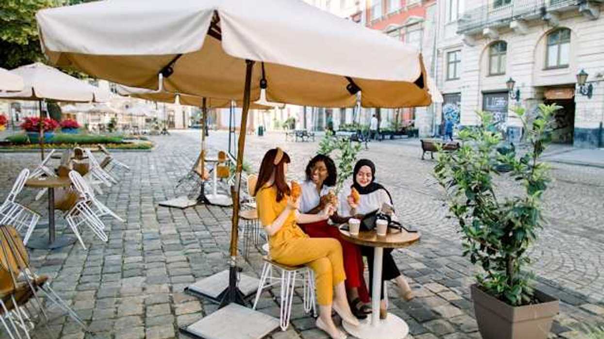 Three women sitting under an umbrella in a European city