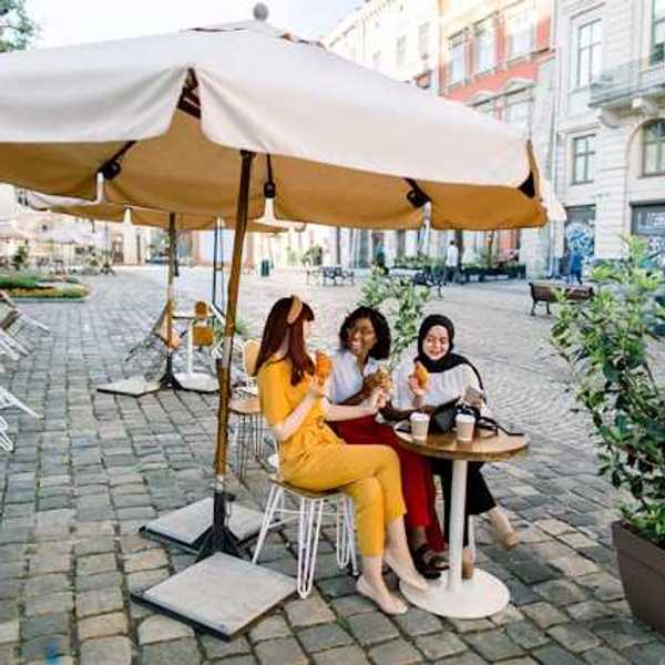 Three women sitting under an umbrella in a European city