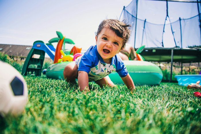 Toddler crawling on grass with plastic toys