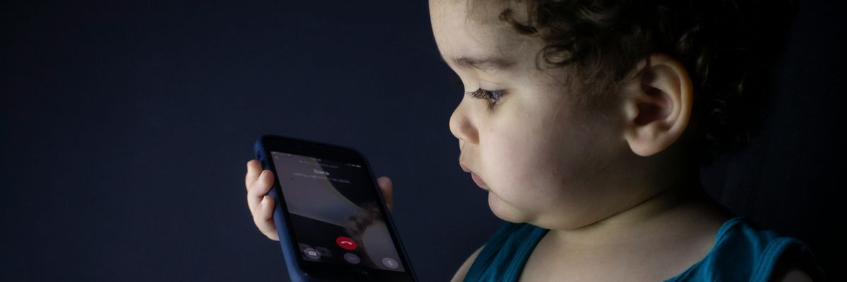Toddler in blue tank top holding black smartphone.