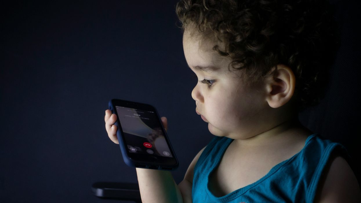 Toddler in blue tank top holding black smartphone.