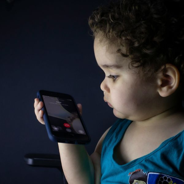 Toddler in blue tank top holding black smartphone.