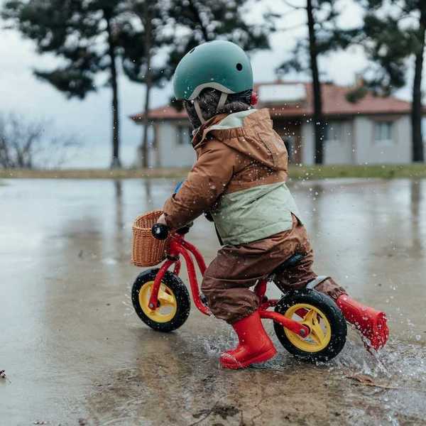 Toddler in red boots riding a red bike in the rain.