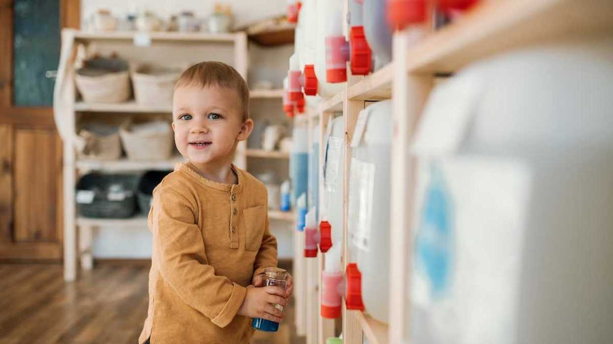 toddler with a refillable container standing next to bulk dispensers in a zero-waste shop