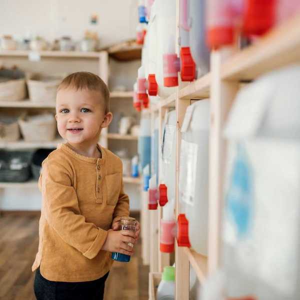 toddler with a refillable container standing next to bulk dispensers in a zero-waste shop