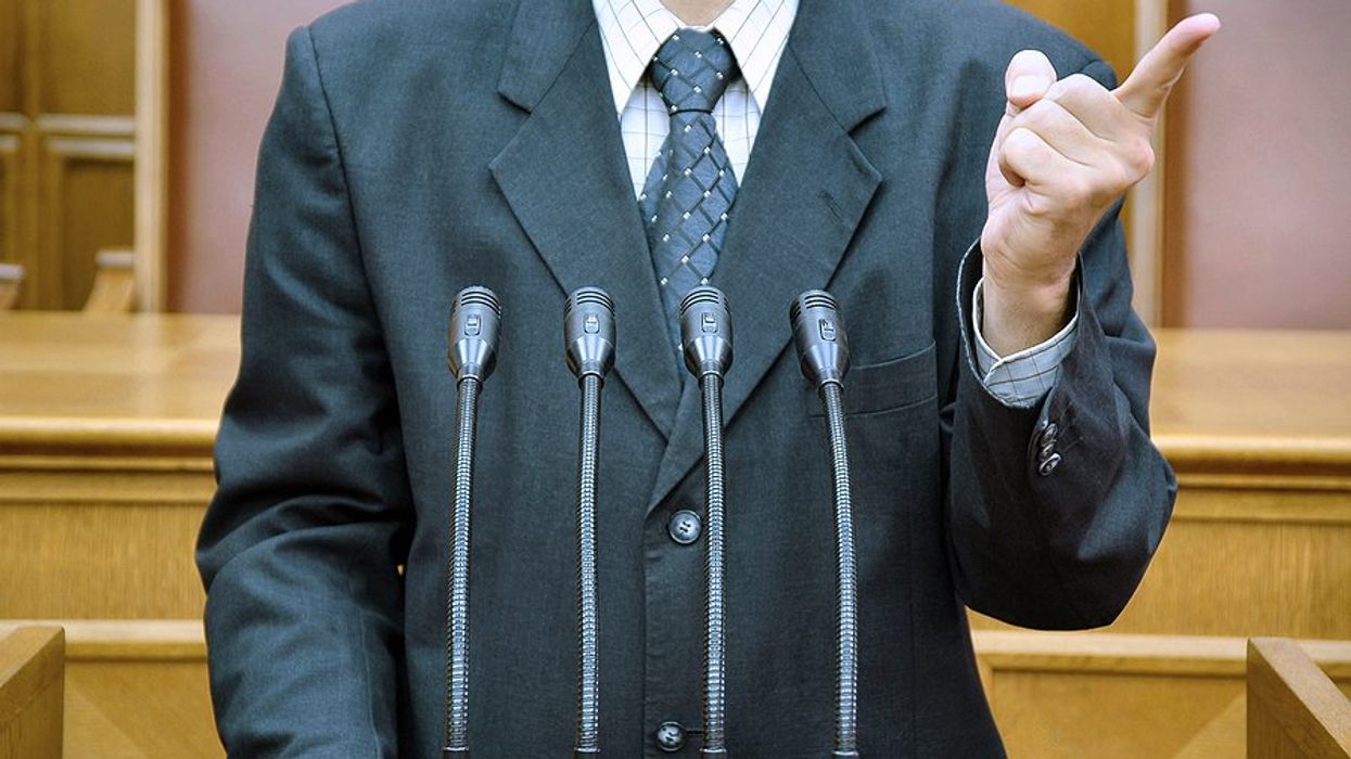 Torso of a politician in a suit standing at a podium shaking his finger.