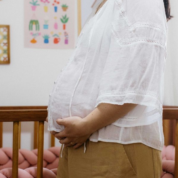 Torso of a pregnant woman standing in front of a baby crib.