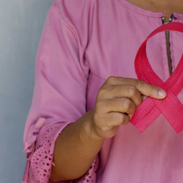 Torso of a woman in a pink shirt holding a pink ribbon commemorating breast cancer awareness.