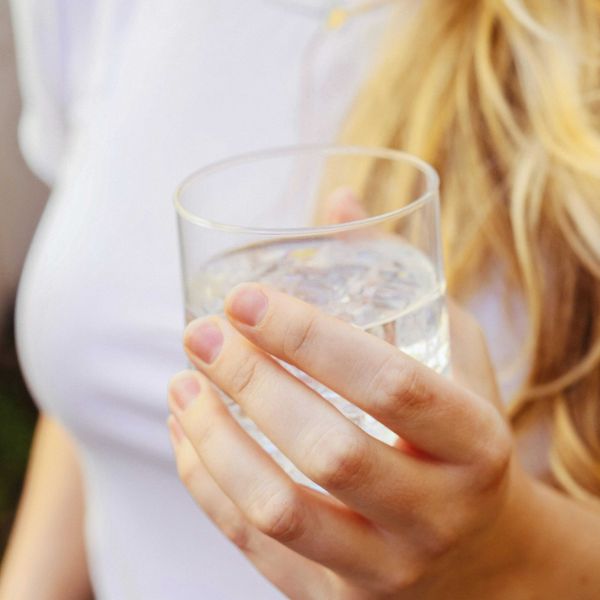 Torso of a woman with blond hair holding a glass of water in her hand.