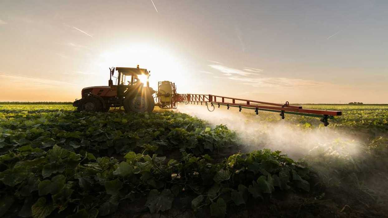 Tractor and driver backlit applying herbicides to crop