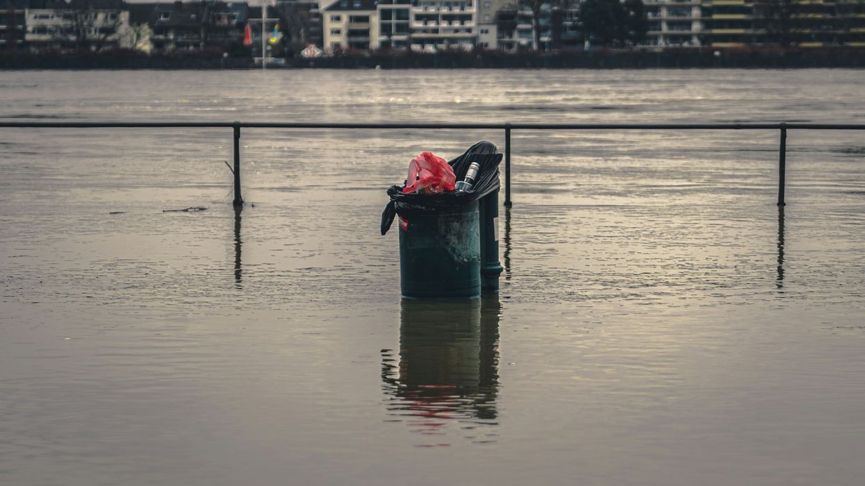 Trash can in the middle of a flooded area of city with buildings visible in distance.