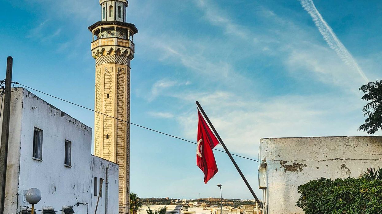 Tunisia flag flying from a building with a tower in background.