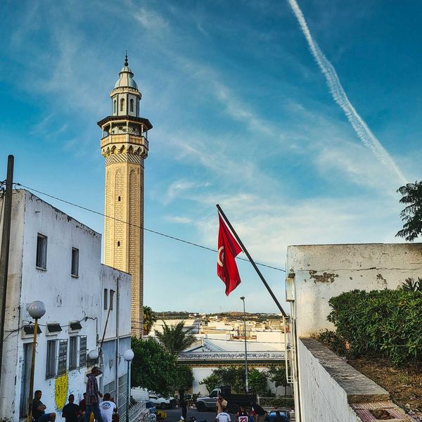 Tunisia flag flying from a building with a tower in background.