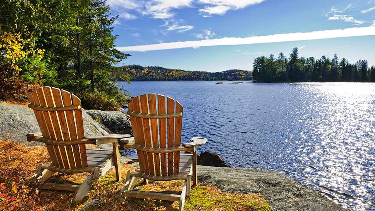 Two Adirondack chairs sitting on the edge of a lake