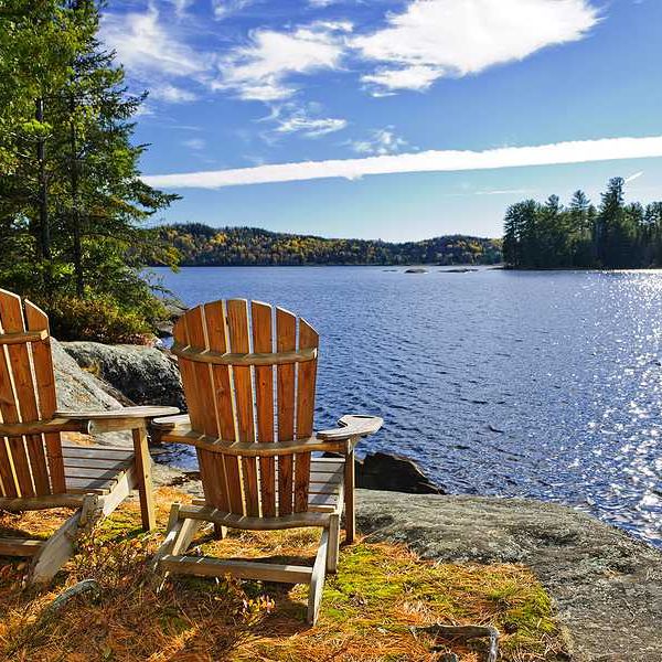 Two Adirondack chairs sitting on the edge of a lake