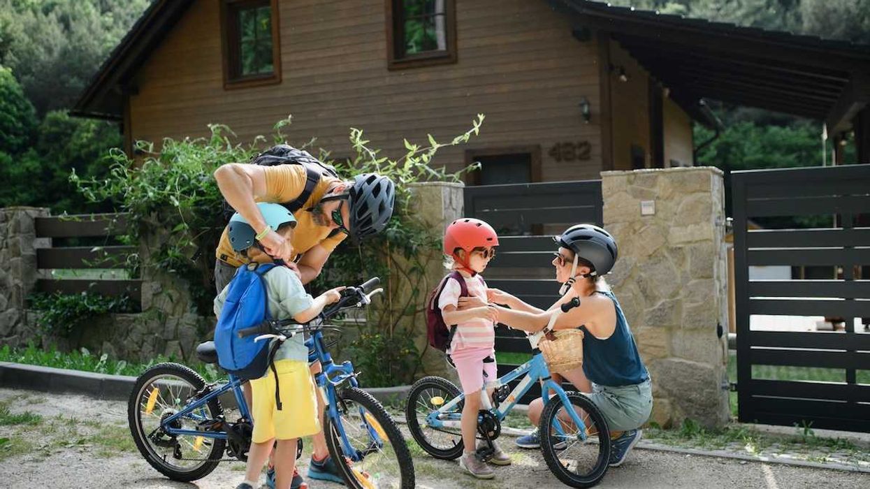 Two adults and two children putting on helmets and backpacks, preparing for a bike ride