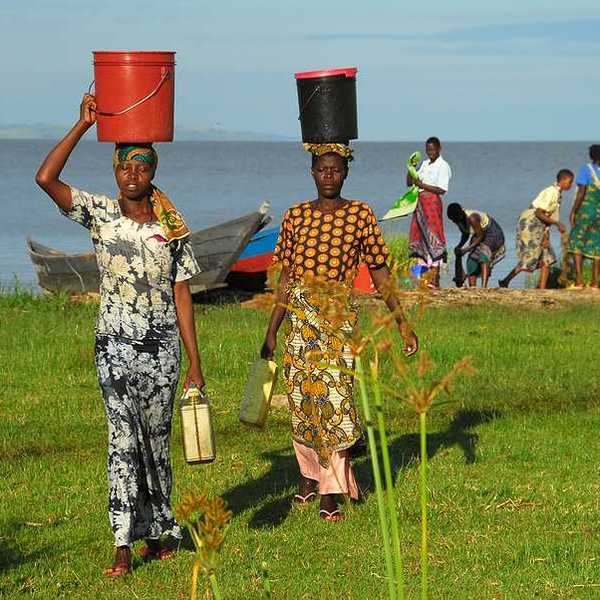 Two African women walking away from Lake Victoria with buckets on their heads