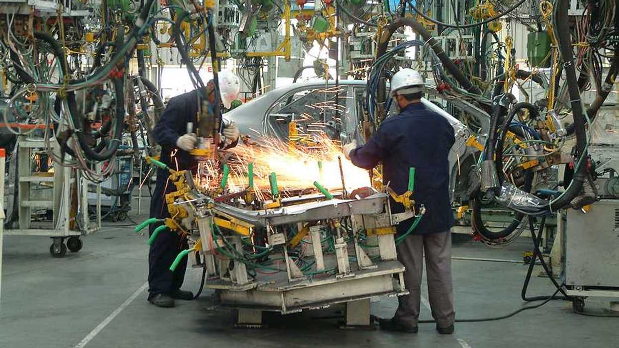 Two automotive workers using machinery to build an engine