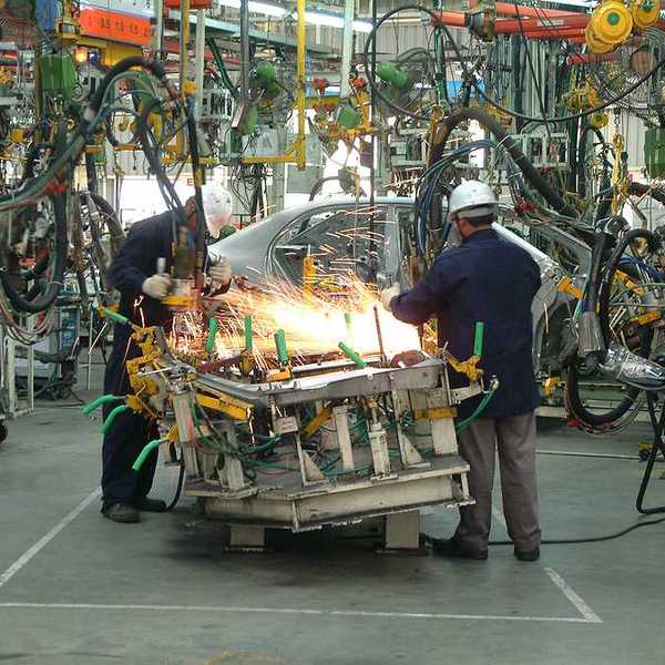 Two automotive workers using machinery to build an engine