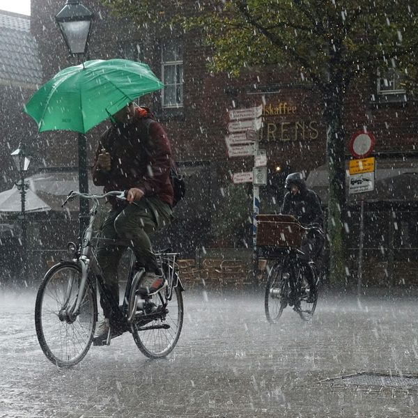 Two bicyclists riding single-file in a downpour