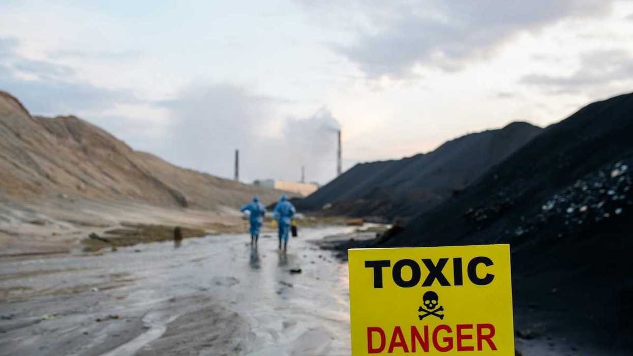 Two blue-suited HazMat clad workers approaching a toxic site. Yellow sign reads "TOXIC - DANGER."