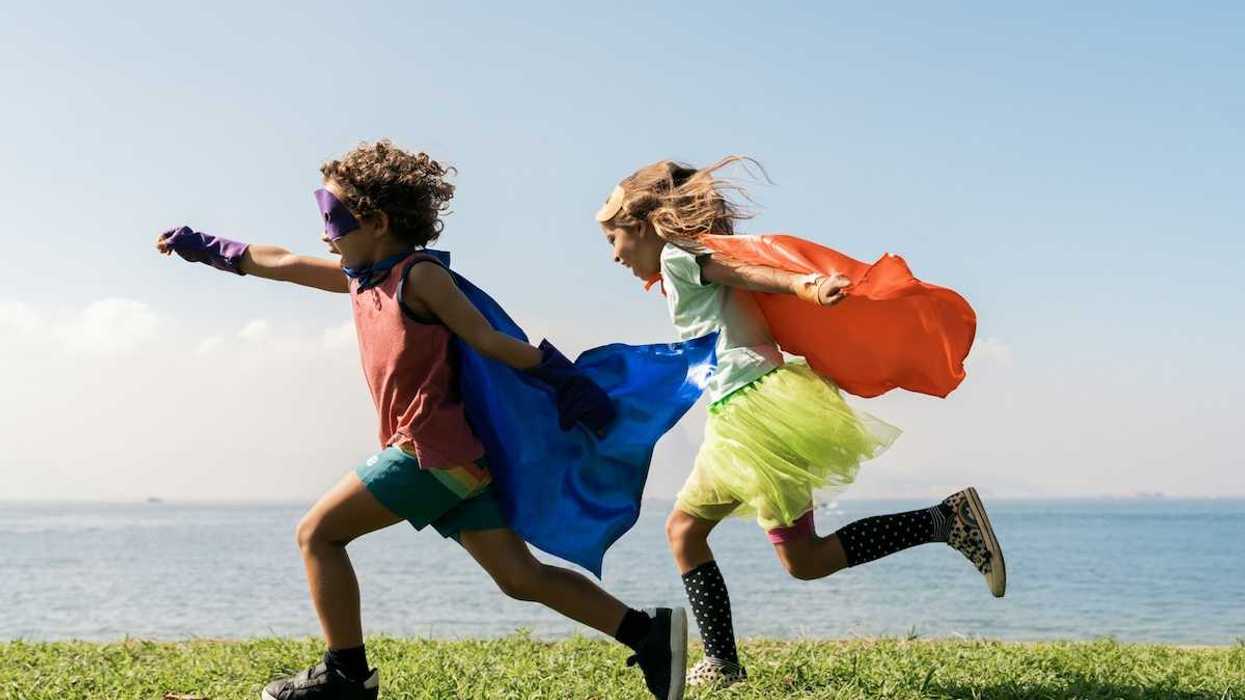 Two children joyously running while wearing capes seemingly pretending to be super heroes