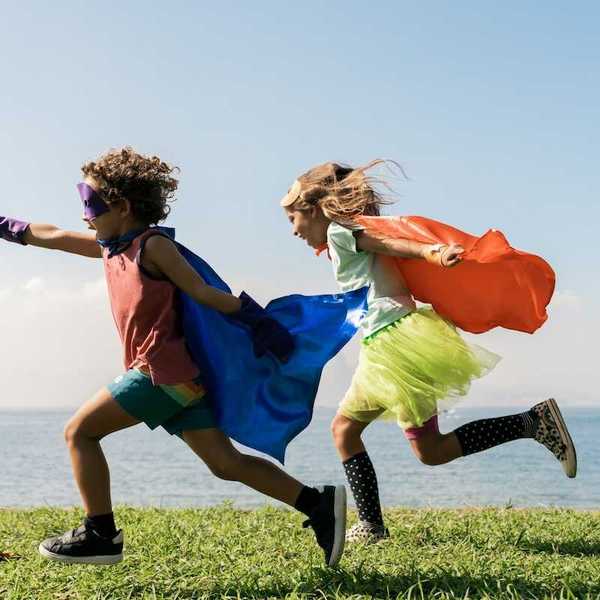 Two children joyously running while wearing capes seemingly pretending to be super heroes
