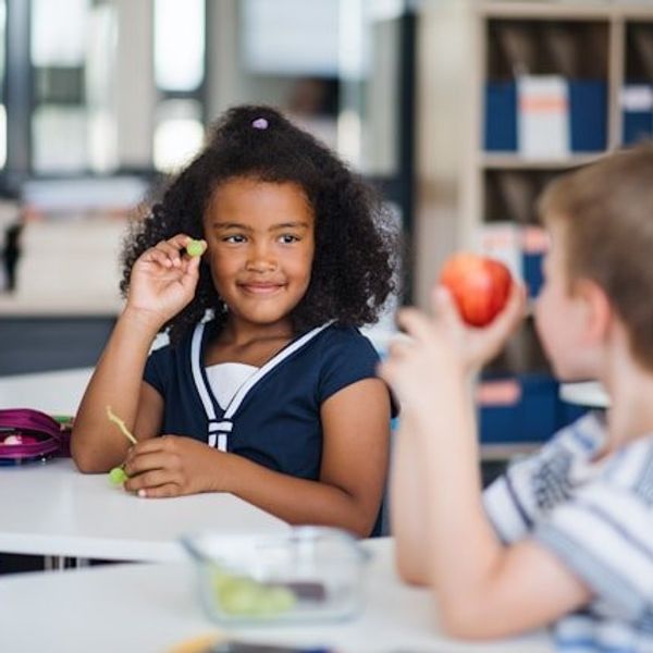 Two children sitting at a table at school eating their lunch