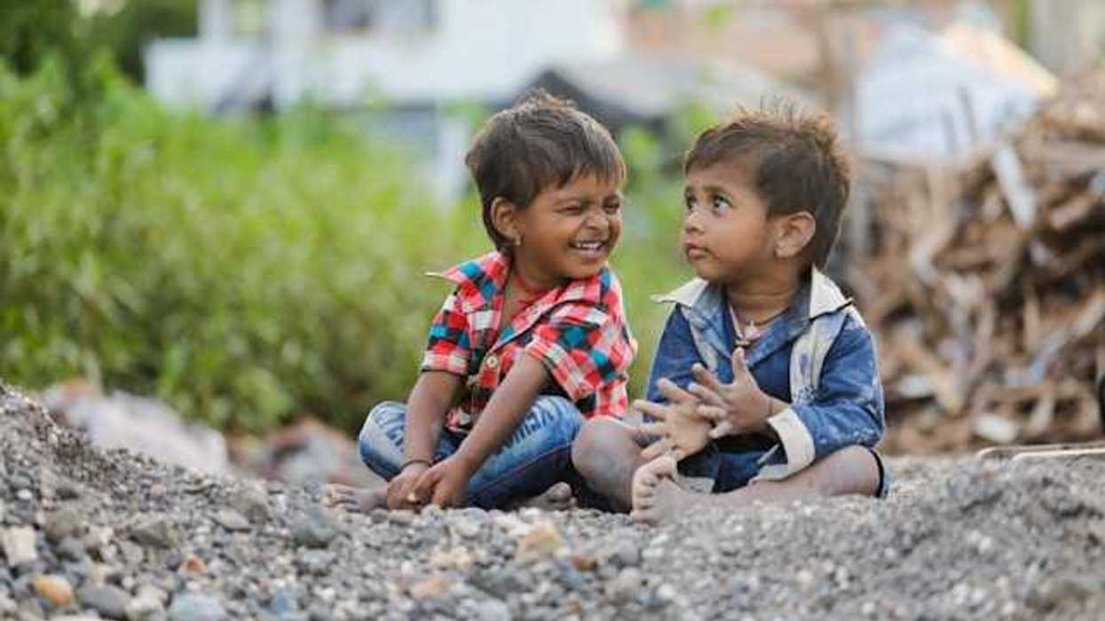 Two children sitting on the gravel, one smiling at the other